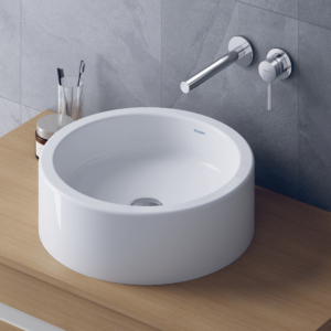 Starck 1 tvättställ för bänk från Duravit i en rund form på en bänkskiva i trä och en väggblandare.