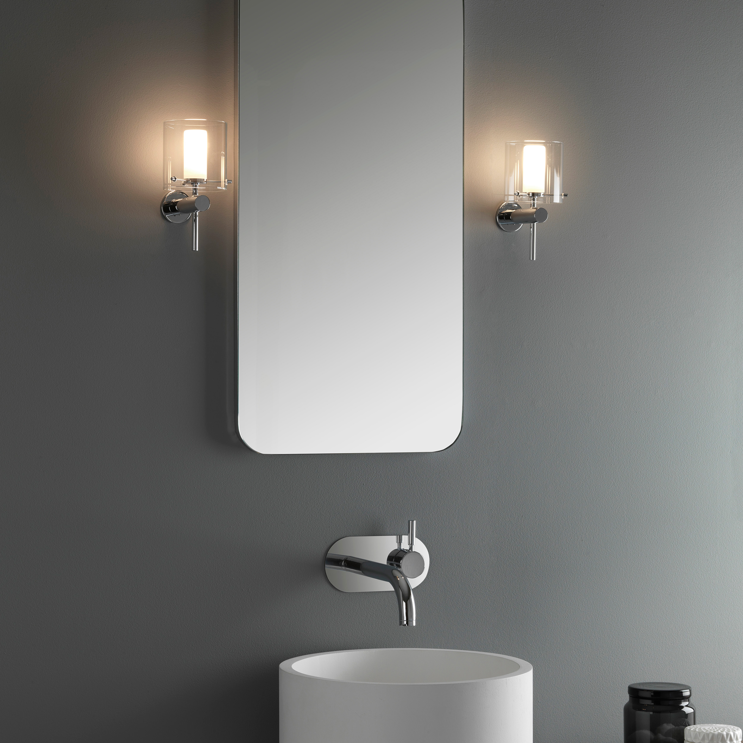 Arezzo vägglampa som sitter på en vägg på vardera sida om en rektangulär spegel.