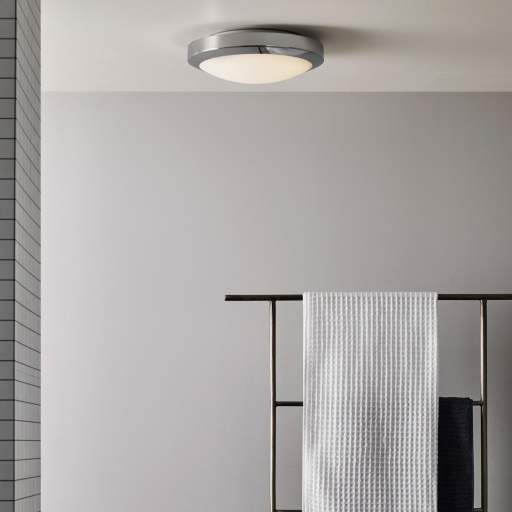 Dakota taklampa sitter i taket i ett badrum, på väggen hänger en hylla med handdukar.