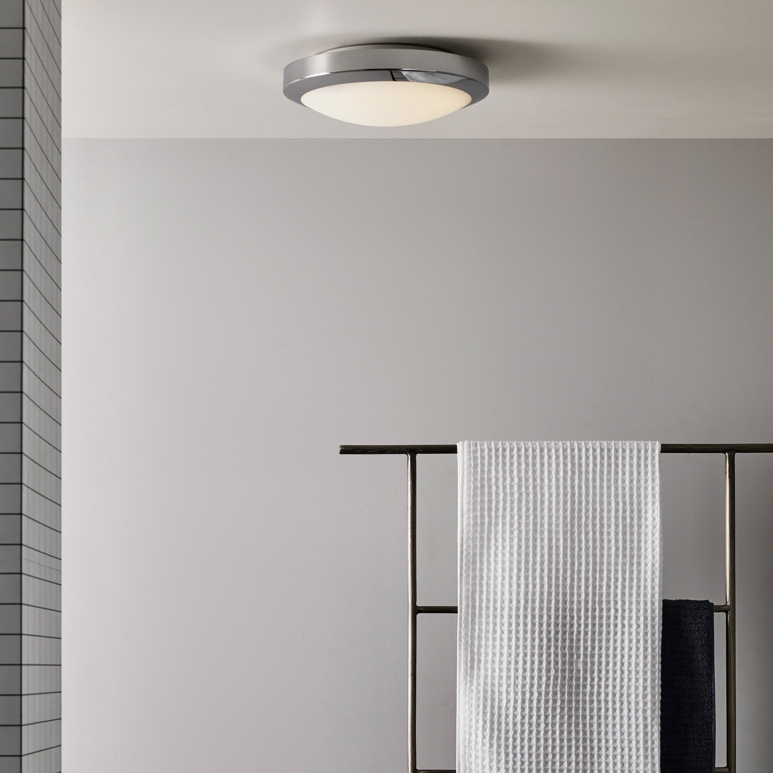 Dakota taklampa sitter i taket i ett badrum, på väggen hänger en hylla med handdukar.