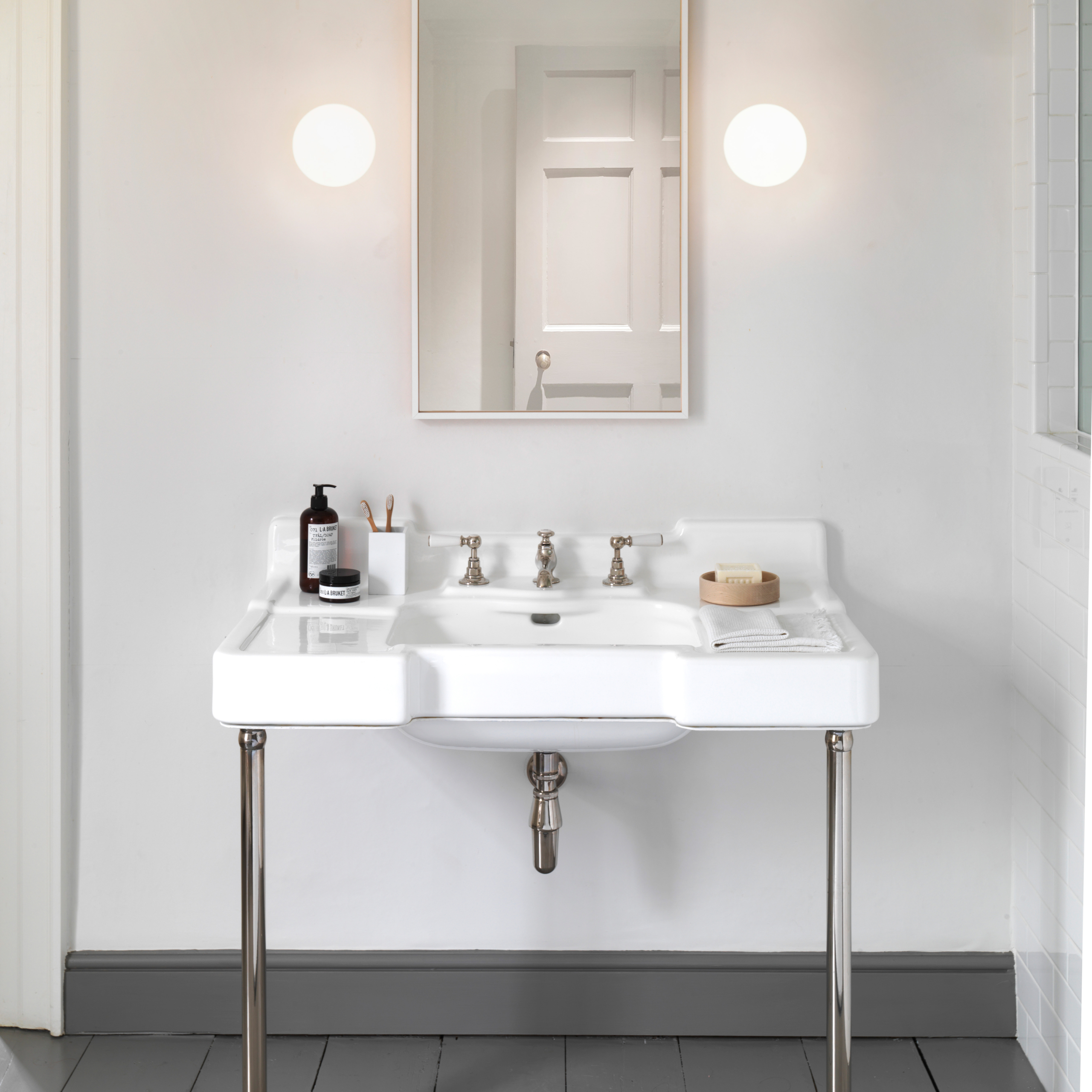 Zeppo Wall rund vägglampa, 2 stycken placerade vid sidan av en rektangulär spegel och under spegeln står ett tvättställ med blandare.