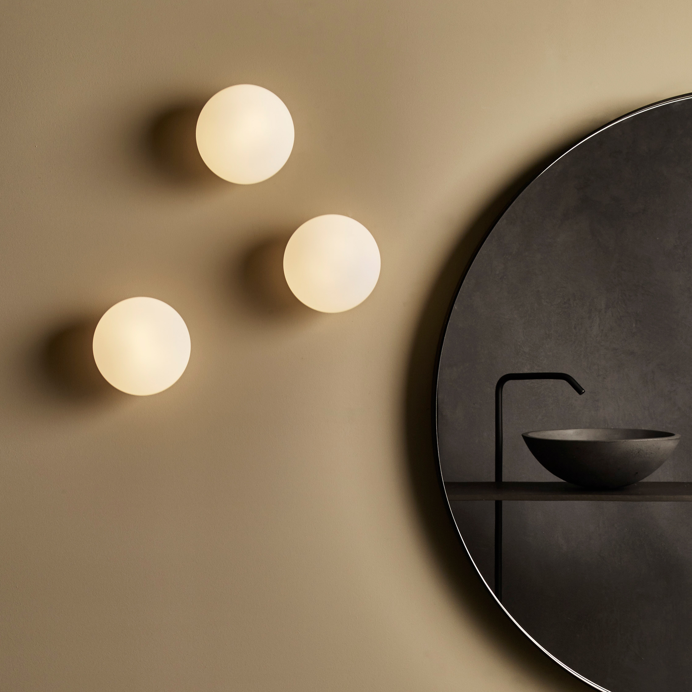 Zeppo Wall rund vägglampa, 3 stycken placerade vid sidan av en rund spegel och under spegeln står ett tvättställ med blandare.