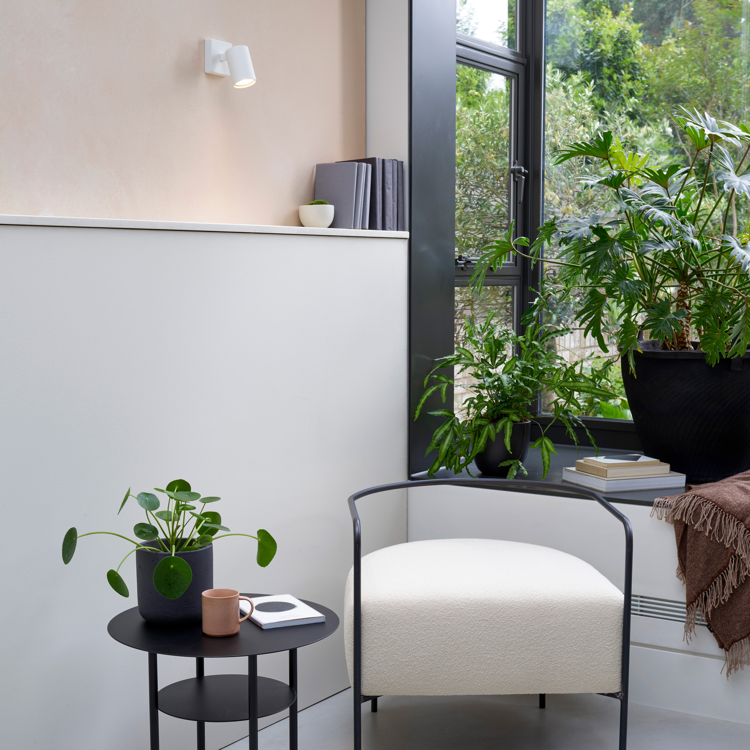 Ascoli Single sittandes på en vägg över en hylla med böcker. På golvet står en fotölj och ett sideboard med blomma och böcker.
