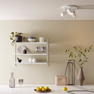 Ascoli Triple Round taklampa med 3 spotlights på en rund bas. under lampan på väggen finns en hylla med glas och ett bord med en skål med citroner.