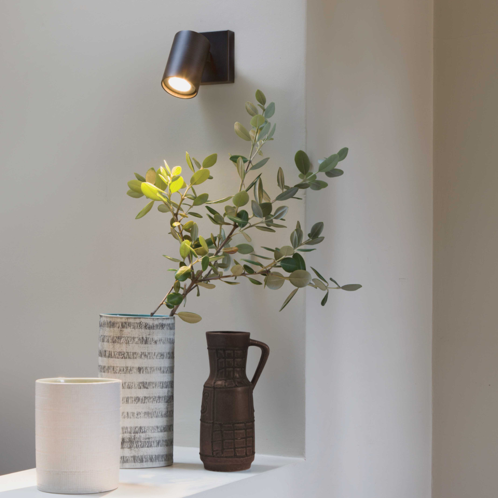 Ascoli Single sittandes på en vägg över ett bord med keramikkrukor och vas med blommor.