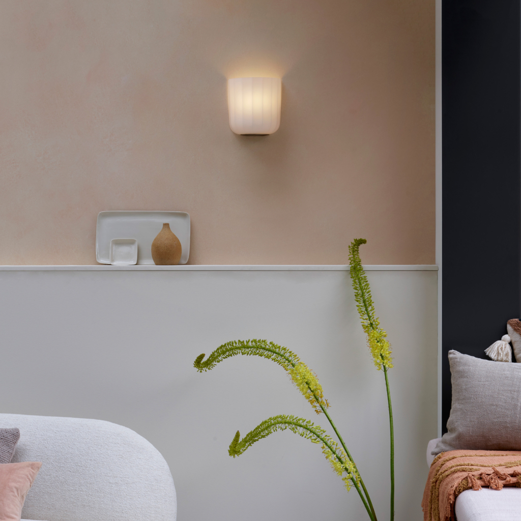 Veo vägglampa sittandes på en ljus vägg i ett rum med soffa och växter.