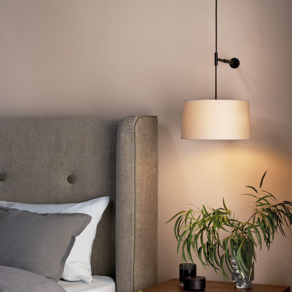 Tapered 320 Pendant lampskärm sittandes på en sänglampa ovanför ett sängbord med blomma och vid sidan om en säng.