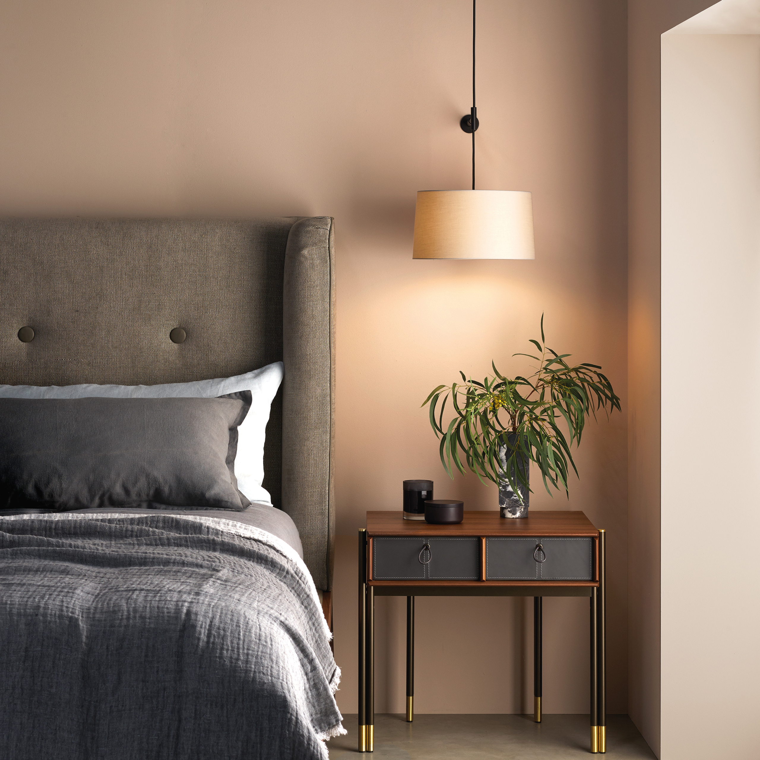 Tapered 320 Pendant lampskärm sittandes på en sänglampa ovanför ett sängbord med blomma och vid sidan om en säng.
