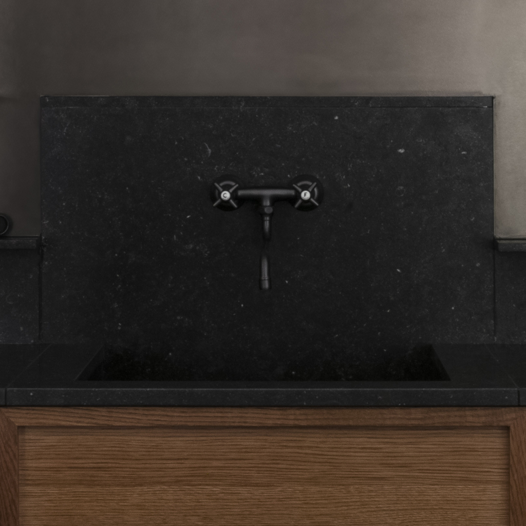 Kök med träskåp med svart stenbänkskiva. Väggköksblandare i en antik stilren design.