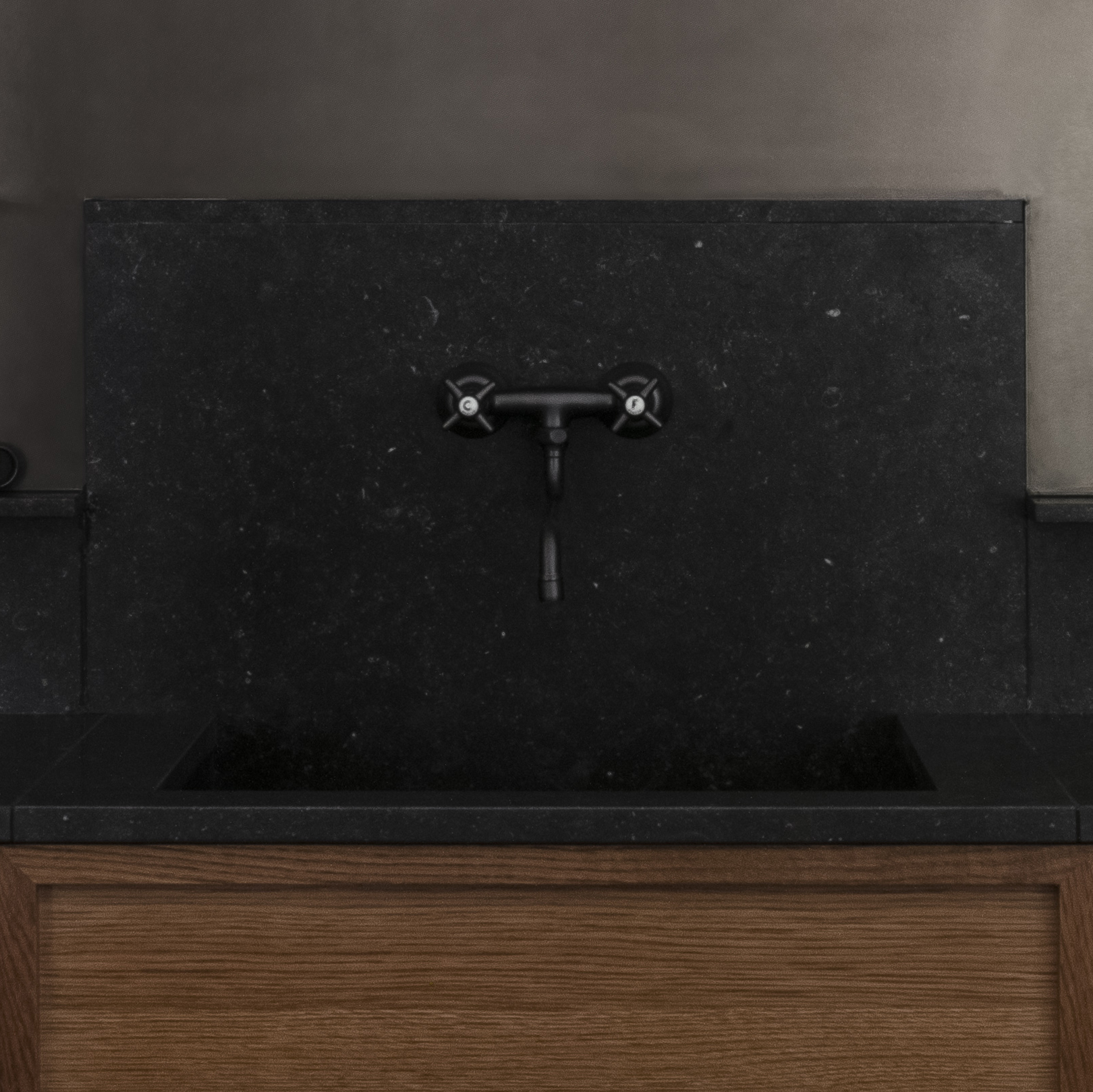 Kök med träskåp med svart stenbänkskiva. Väggköksblandare i en antik stilren design.
