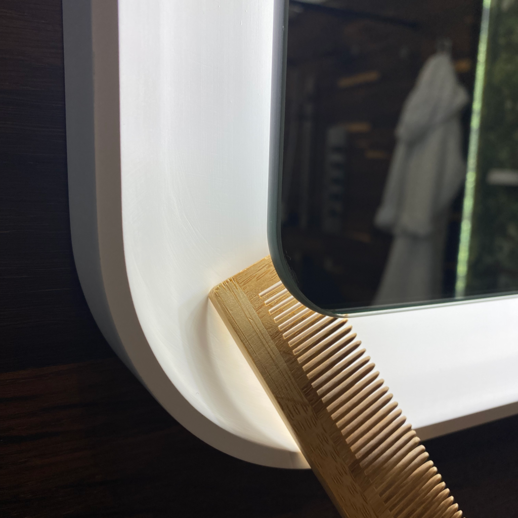 Elegant rektangulär väggspegel sittandes på en trävägg närbild med en träkam som visar distansen i spegelns ram.