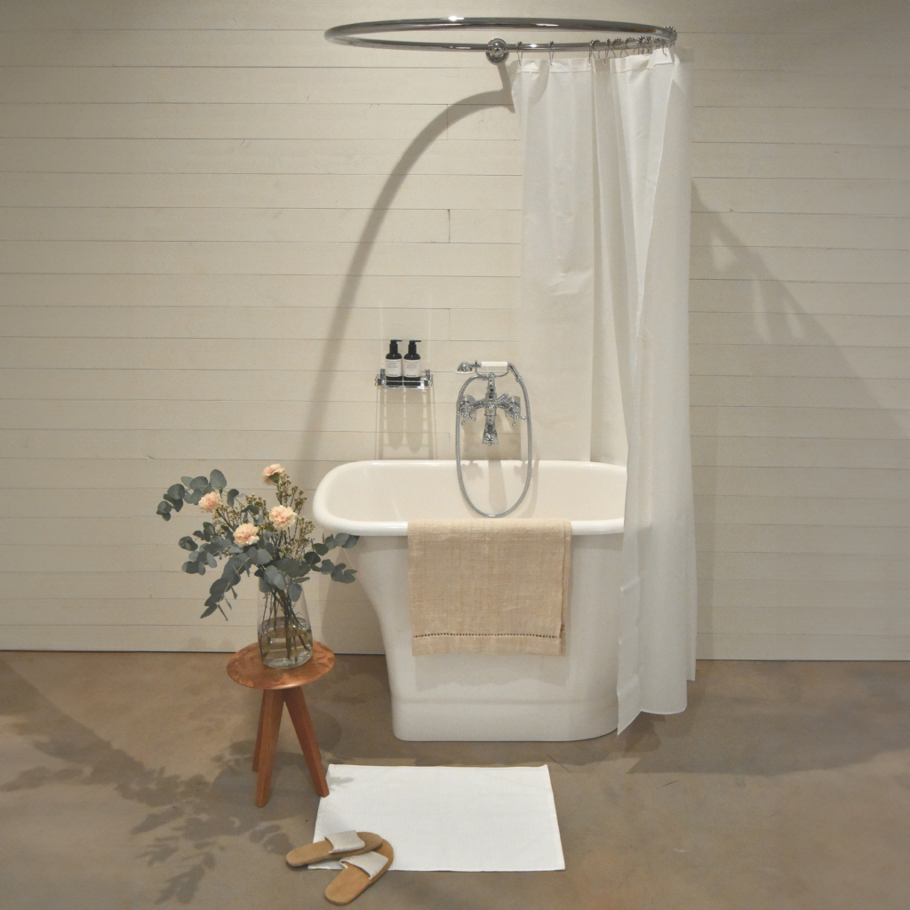 Badrum med vitt sittbadkar, kromad handdukstork emd en handduk, sittpall med en bukett liljor ovanpå. Dusch och badkarsblandare är i en romantisk stil.