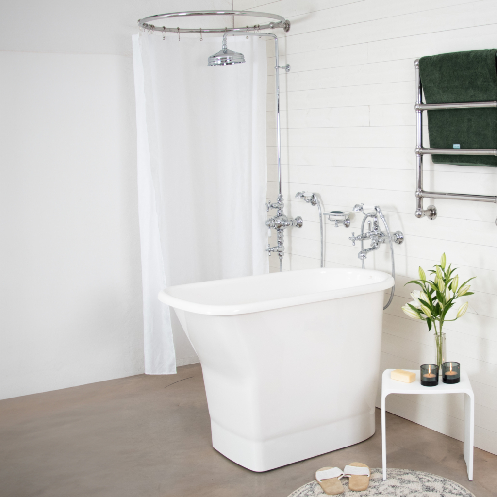 Monaco sittbadkar. Badrum med vitt sittbadkar, kromad handdukstork emd en handduk, sittpall med en bukett liljor ovanpå. Dusch och badkarsblandare är i en romantisk stil.