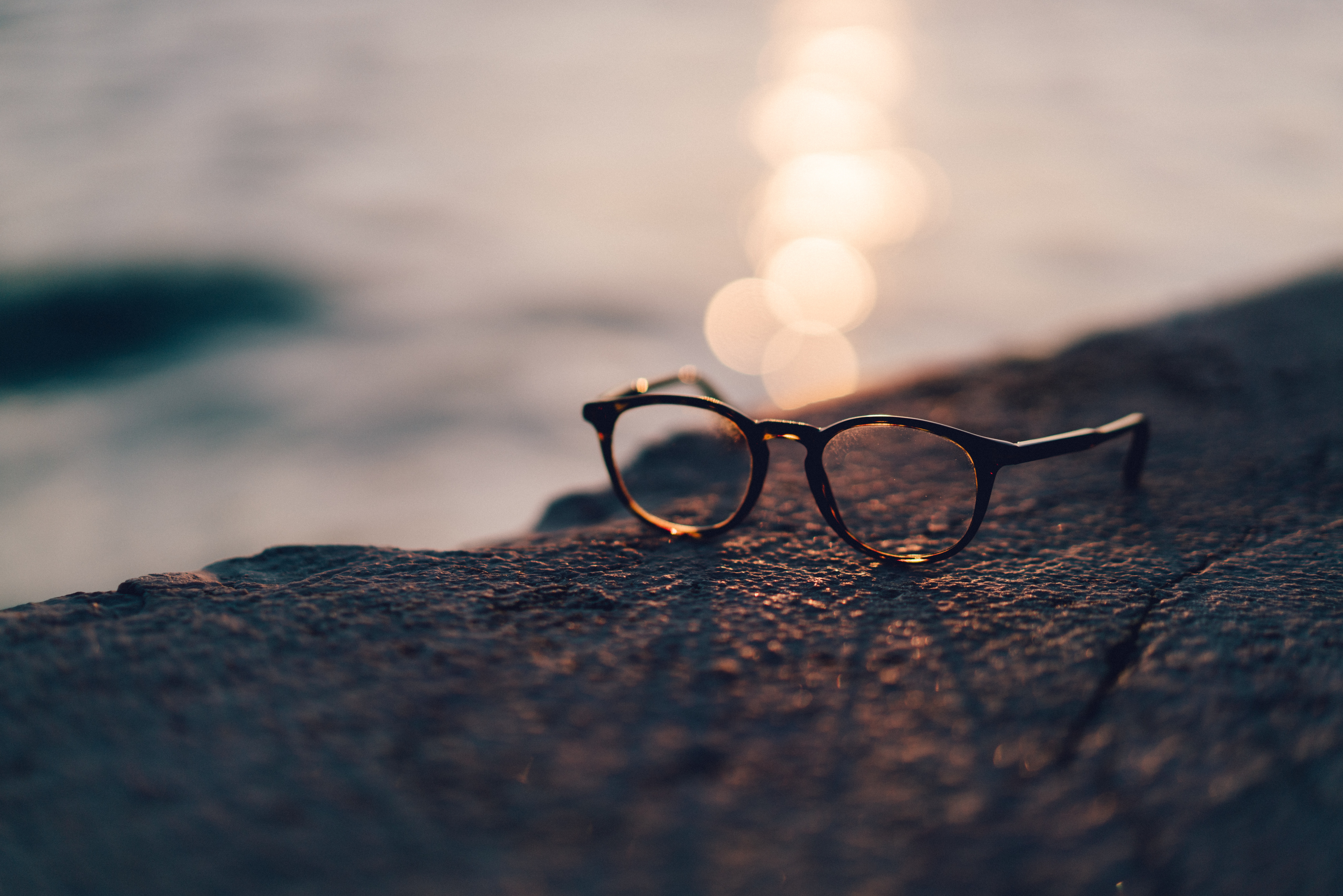 Glasögon som ligger på en klippa med vatten och solnedgång i bakgrunden.