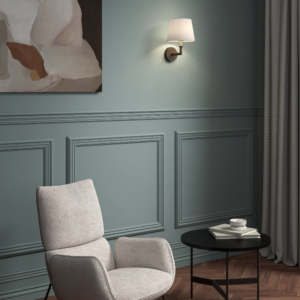 Club Wall vägglampa med lampskärm som sitter på en vägg i ett rum med fåtölj, litet runt bord och en tavla bredvid lampan.