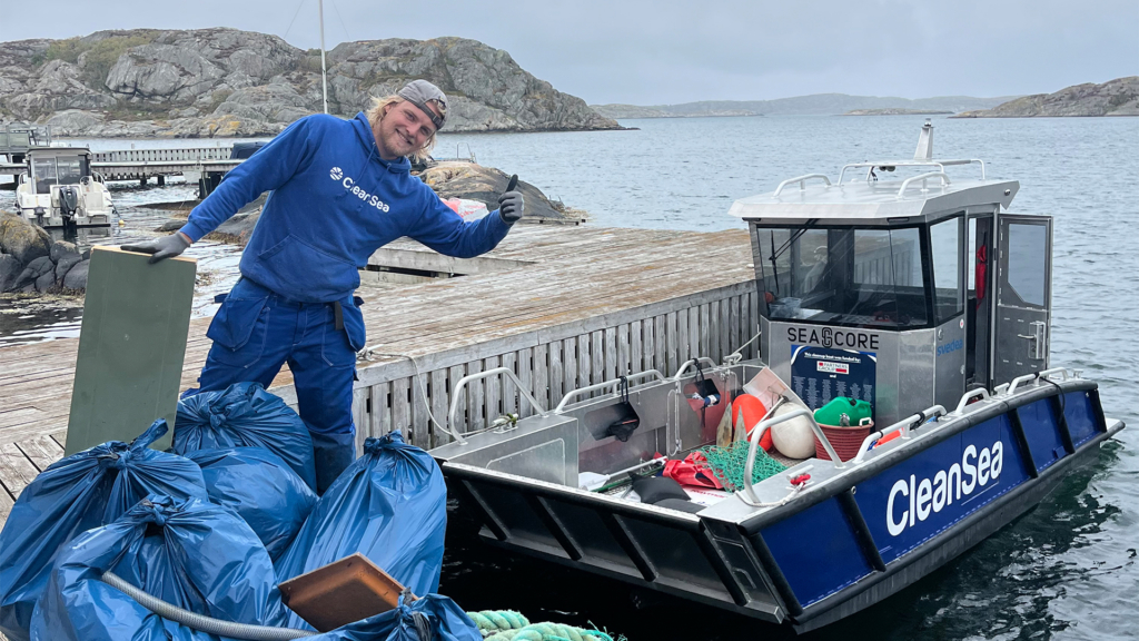 En en kille klädda i blå hoodie vid sin båt full av skräp.