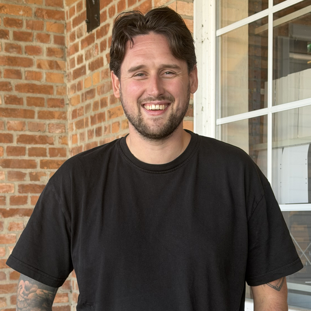 Kille med brunt går och stor leende. Klädd i svart t-shirt.